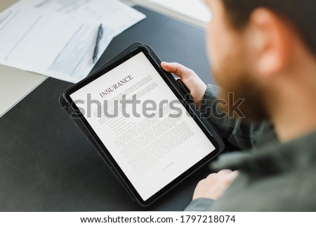 Economist reading insurance on tablet screen at cabinet. Concept of bureaucratic literacy and safety. Man browsing document by modern gadget. Royalty-Free Stock Photo #1797218074