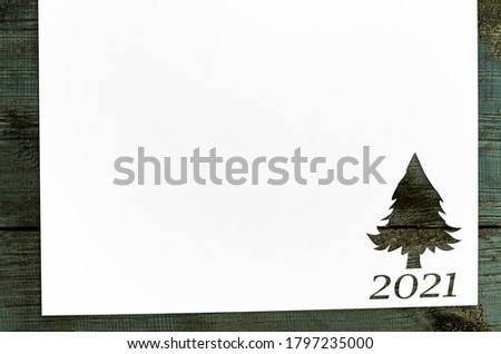 Christmas background. White paper with fir-tree shape cut for new year 2021 card on wooden table