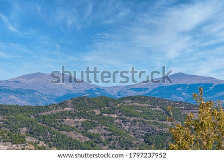 mountainous landscape in the south of Spain, the mountain is covered with vegetation and trees, the sky is blue with clouds
