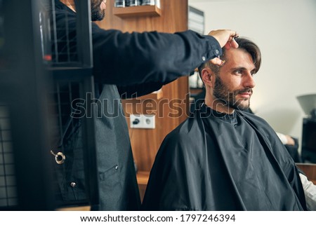 Serious brunette male person being deep in his thoughts while waiting for stylish haircut