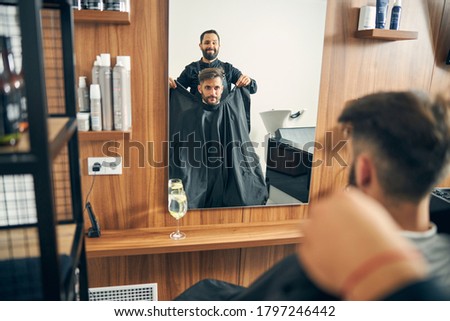 Positive delighted bearded man working in barbershop and communicating with visitors
