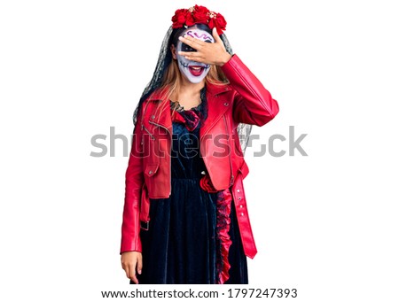 Woman wearing day of the dead costume over background peeking in shock covering face and eyes with hand, looking through fingers with embarrassed expression. 