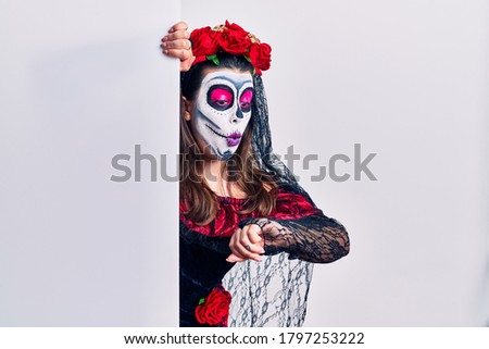 Young woman wearing day of the dead custome holding blank empty banner looking at the watch time worried, afraid of getting late 