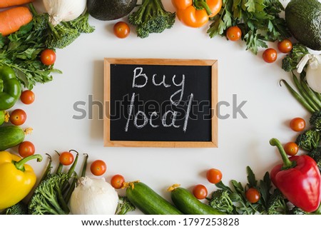 Blackboard with chalk text "Buy Local" on white background and variety of fresh seasonal vegetables, top view. Local farm business