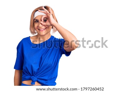 Young blonde woman wearing sportswear doing ok gesture with hand smiling, eye looking through fingers with happy face. 