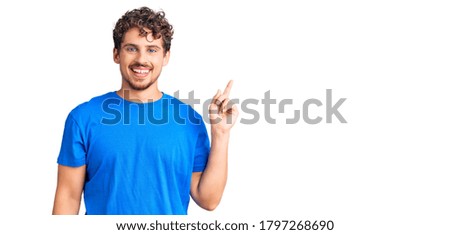 Young handsome man with curly hair wearing casual clothes with a big smile on face, pointing with hand finger to the side looking at the camera. 
