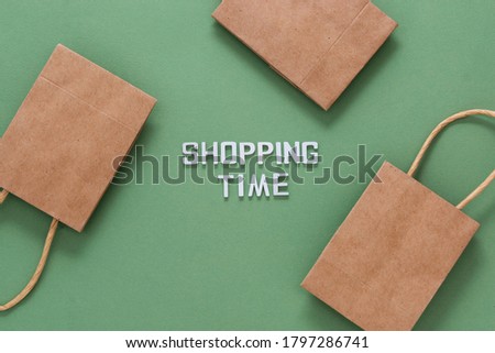 Shopping time inscription with craft brown paper shopping bags isolated on green background. Top view.