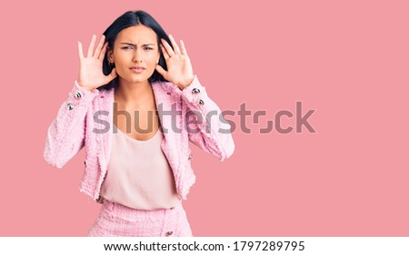 Young beautiful latin girl wearing business clothes trying to hear both hands on ear gesture, curious for gossip. hearing problem, deaf 