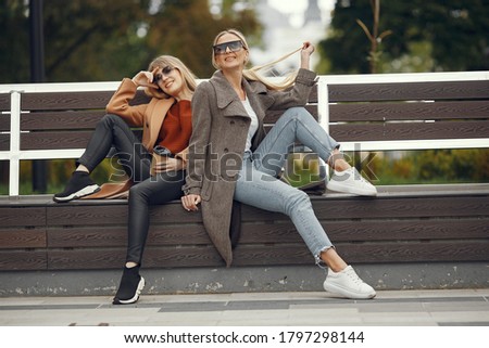 Beautiful girls sitting on a bench. Women in a spring city. Ladies drinking a coffee.