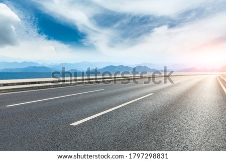 Asphalt road and lake with mountains under blue sky.