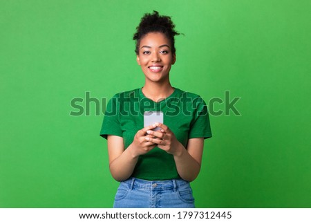 Cool Application. Smiling african lady using smart phone on green studio background and looking at camera