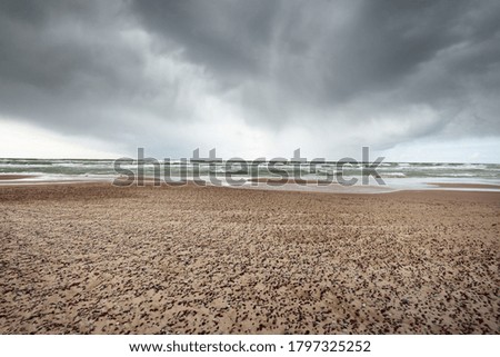Sandy shore of the Baltic sea under the dramatic clouds after thunderstorm. Ventspils, Latvia. Epic seascape. Cyclone, gale, storm, rough weather, meteorology, climate change, natural phenomenon