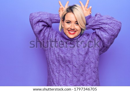 Beautiful blonde plus size woman wearing casual turtleneck sweater over purple background Posing funny and crazy with fingers on head as bunny ears, smiling cheerful