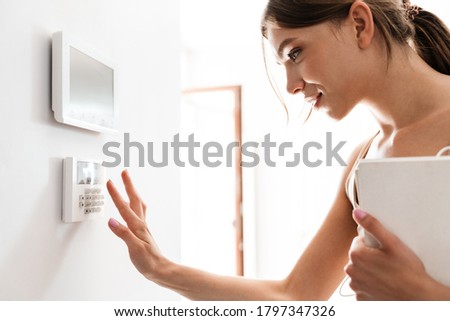 Young woman entering code on keypad of home security alarm Royalty-Free Stock Photo #1797347326