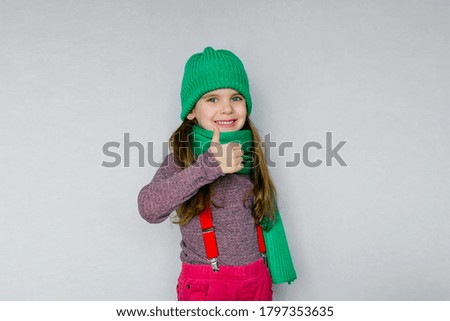 Blonde kid child girl is dressed in a warm sweater, scarf and beanie on a grey background. Fight the cold. Winter and autumn seasons. Concept of children's health, vitamins, medicines.