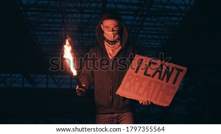 Young man solitary street protests stands with sign I Can't Breathe on cardboard, lights up with signal flare in hand background of industrial night. I Can't Breathe protests in USA, Europe. Freedom