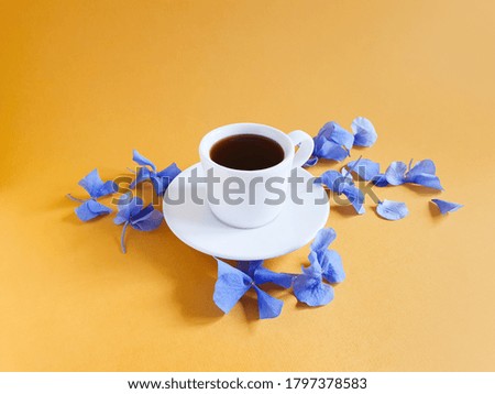 A cup of coffee / hot chocolate and blue hydrangea flowers on a textured bright yellow orange background. Copy space, mockup. Aroma and good morning concept.