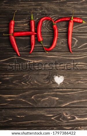 top view of word hot made of chili peppers near salt heart on wooden surface