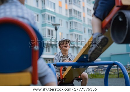 four cute little caucasian boy balancing on seasaw at the playground. Backs of other kids on foreground. Appartment building on background