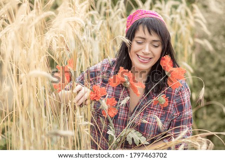 Beautiful woman farmer 40 years old rejoices in the harvest of wheat in the field among the ears and poppies. Summer time, autumn. Working in the process