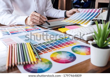 Image of male creative graphic designer working on color selection and drawing on graphics tablet at workplace with work tools and accessories.