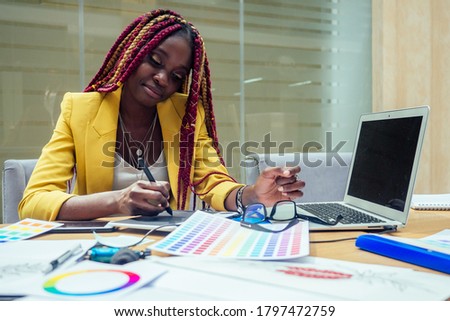 woman fashion designer with afro pigtails dreadlocks working on her atelier or print publishing house and graphic designer draws a sketch on a tablet. cosmetic distributor working in the office