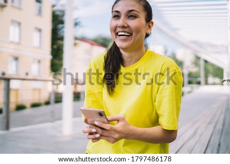 Happy asian woman holding mobile phone laughing at funny social media content on free time, smiling hipster girl 20s enjoying sharing content on smartphone using 4G connection on city street