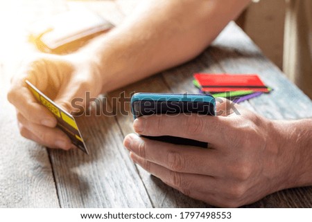A man holds a credit card in his hands and uses a mobile phone close-up, paying for purchases in online stores, internet banking and internet marketing