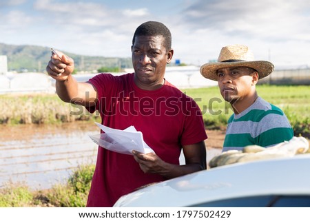 Portrait of african and hispanic male gardeners with papers discussing and gesturing outside