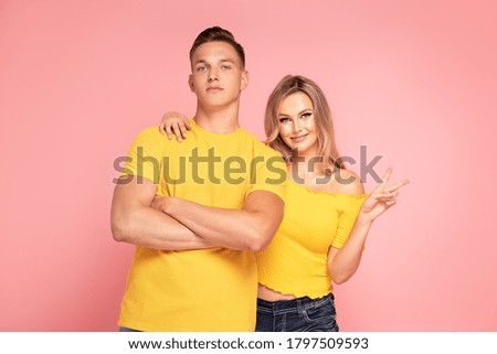Beautiful young couple smiling, posing on pink pastel studio background.