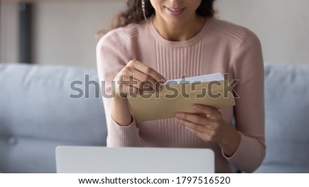 Crop close up of young Caucasian woman hold paper envelope open read postal mail letter at home, female receive post paperwork or document, consider notice or notification correspondence news Royalty-Free Stock Photo #1797516520
