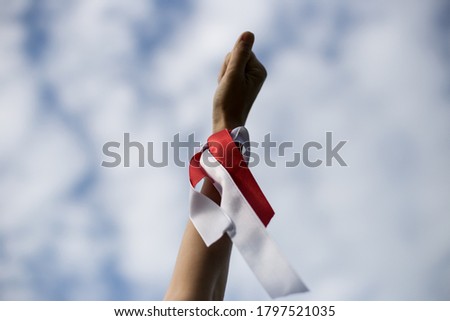 The girl raises her hand high into the sky. White-red ribbon as a symbol tied on the wrist