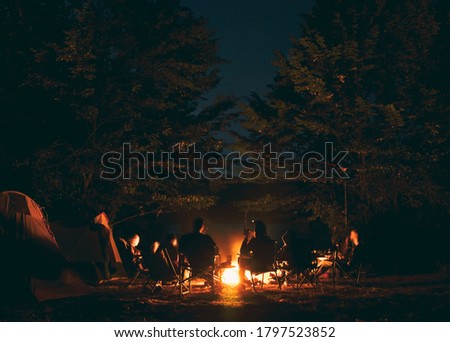 The group of young people are sitting around the bonfire and talking and singing songs Royalty-Free Stock Photo #1797523852