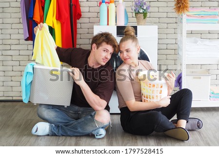 Portrait of young happy Caucasian couple sitting in front of washing machine ready to wash their clothes at home Couple lifestyle spending time doing laundry together and activity 