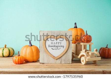 Happy Thanksgiving concept with photo frame, toy truck and pumpkin decor on wooden table over blue background. Autumn season greeting card.