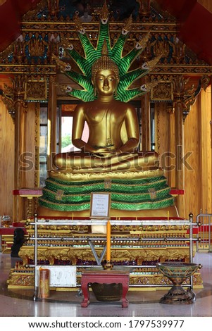The top golden Buddha statue has a green serpent.There are 9 naga heads.There is a large incense burner and candles.The photo of the Buddha image in a temple in Thailand.It is sacred.Buddhists respect