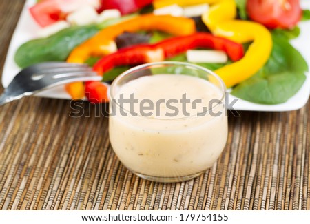 Horizontal photo of a small glass bowl filled with creamy Italian dressing with salad on white plate in background  Royalty-Free Stock Photo #179754155