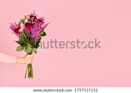 Female hand hold beautiful bouquet of flowers isolated on pink background. Woman holding bouquet with roses and eustoma flowers.