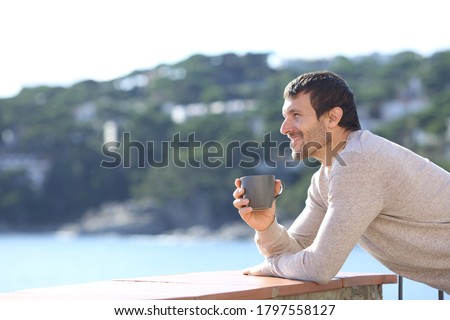 Side view of a happy man contemplating views with coffee cup on a balcony on the beach Royalty-Free Stock Photo #1797558127