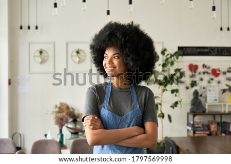 Smiling confident African American young woman with Afro hair modern cafe small business owner, female waitress in restaurant looking away standing arms crossed in cozy coffee shop interior. Portrait. Royalty-Free Stock Photo #1797569998