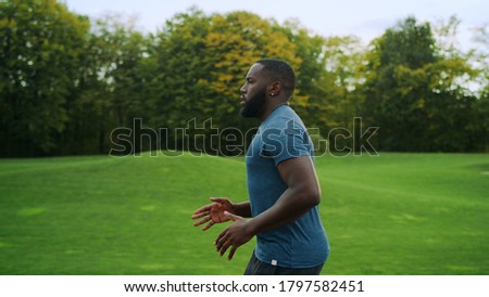 Side view sporty man jogging in green park. Handsome sportsperson exercising outdoors in slow motion. Male runner doing cardio workout on road in morning. African man running outdoors