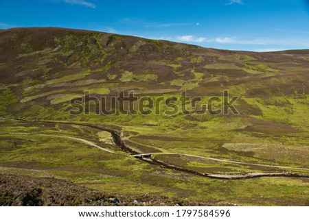 A landscape image from an elevated view on a hillside looking across Glen Callater in the Scottish Highlands to the green and heather covered hills opposite.