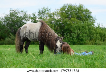 The Caucasian young woman is lying next to her pony in the grass.