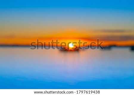 Abstract deliberate defocus coastal background for travel or coastal effects use sunrise over blue water of Tauranga harbour with intense golden glow on horizon.