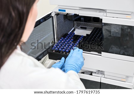 Scientist in a white lab coat putting vial with a sample into autosampler of HPLC system. High performance liquid chromatography at chemical laboratory. Developing of pharmaceuticals or vaccine Royalty-Free Stock Photo #1797619735