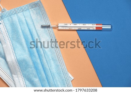 flat lay of thermometer and mask on a blue and orange background. covid 19. Concept disease and cure