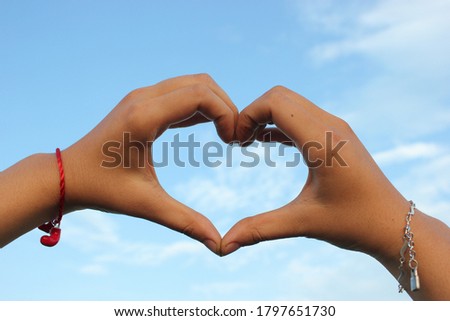 Two hands make heart shape with blue sky and clouds background 