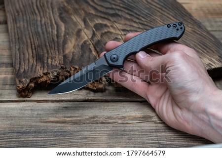 Folding knife with carbon handle. Small sharp knife in hand. Front view.