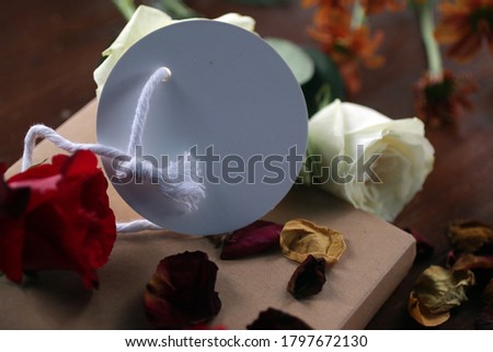 White and red roses, dried petals with blank tag label paper for your notes on a gift of a book on messy table.  Still life concept with natural floral background.