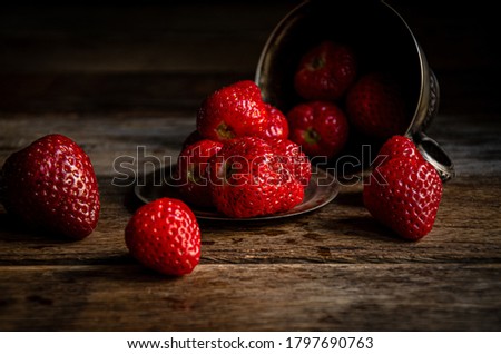 Strawberries overturned from a silver cup on wooden boards.
